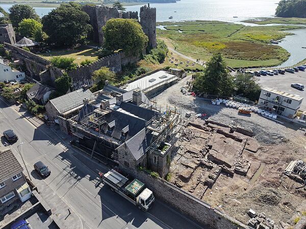 Island House beside the castle's outer wall, with the round tower of Laugharne Castle and the Taf estuary beyond.