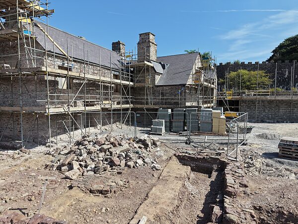 The rear elevation of Island House under scaffolding, with excavated ground and stone in the foreground.