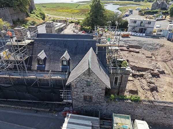 Close aerial view of the dormer windows and chimneys of Island House during roof works, with the estuary beyond.