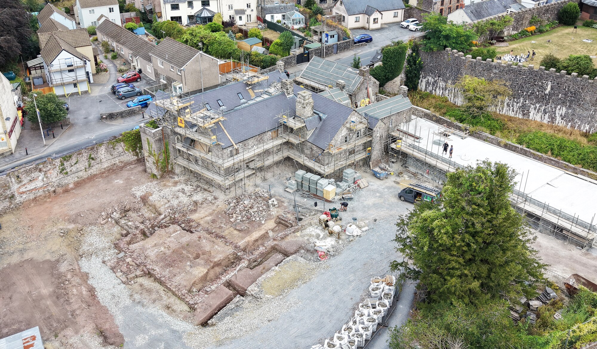 Island House from the air: the house under restoration filling the frame with its new slate roof, the excavated medieval foundations laid bare in the yard in front of it, the castle's curtain wall to the right and the town of Laugharne behind.