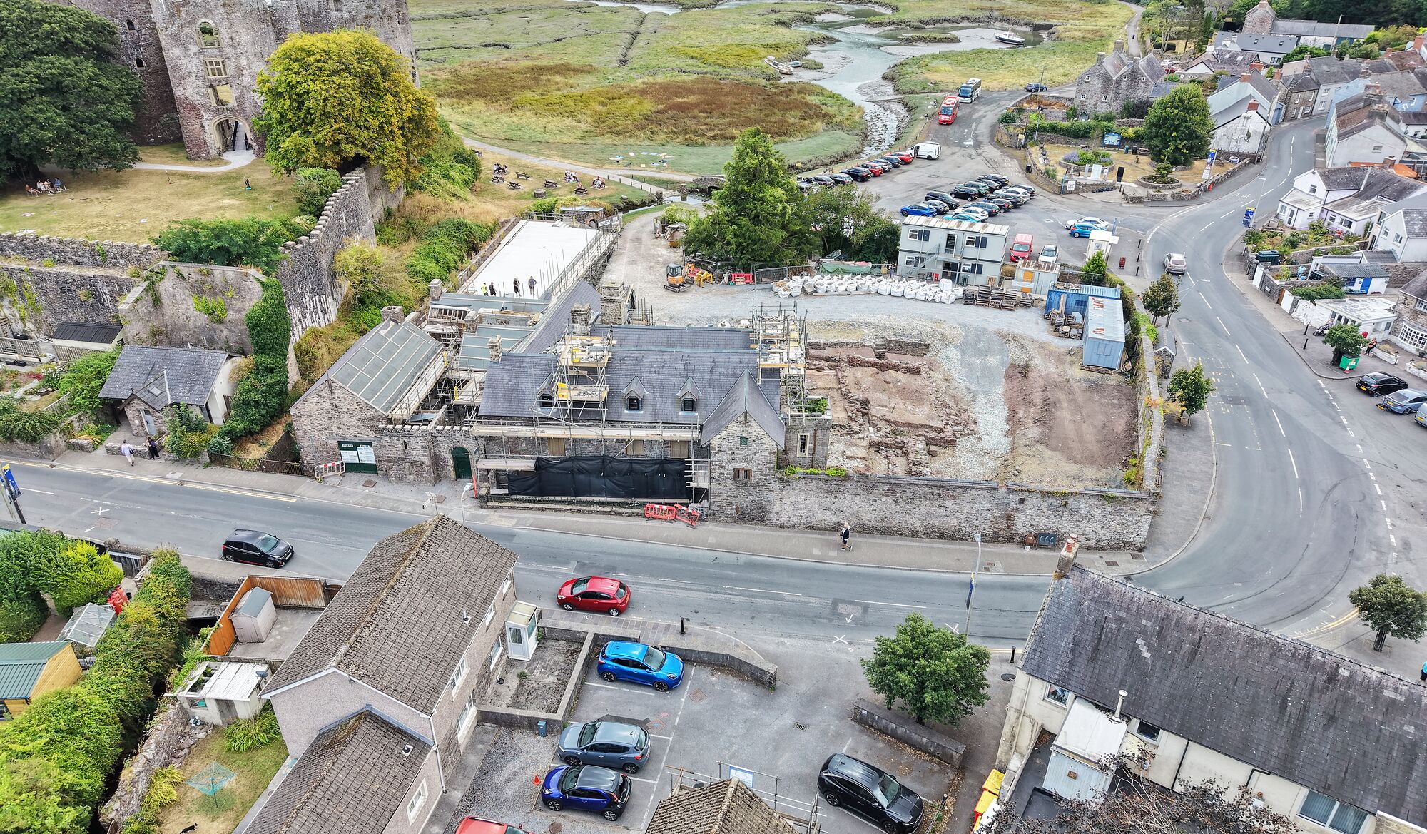 Island House from the air: the whole house under restoration below the wall of Laugharne Castle, with the town to one side and the Taf estuary and marshes beyond.