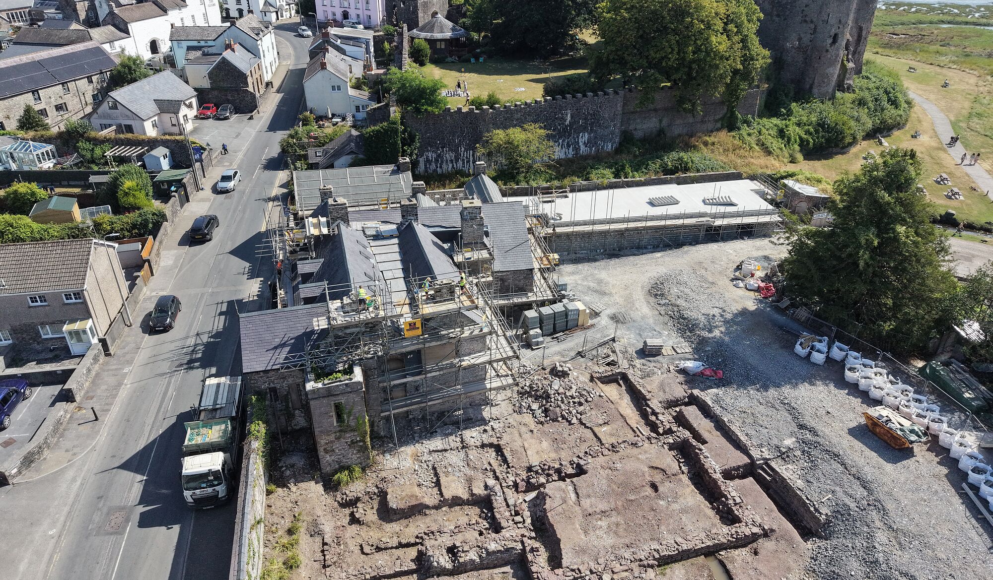 Island House from the air, seen over Wogan Street with Laugharne Castle behind it and the Taf estuary beyond. The house is under scaffolding and the ground around it has been excavated.
