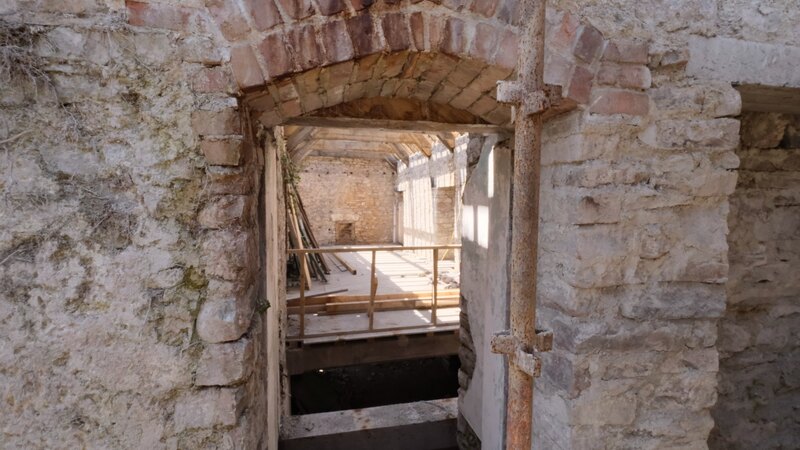 The arched doorway at Island House today: a stone opening under a brick-dressed relieving arch, its jambs cut from dressed stone, looking through into the beamed space beyond.